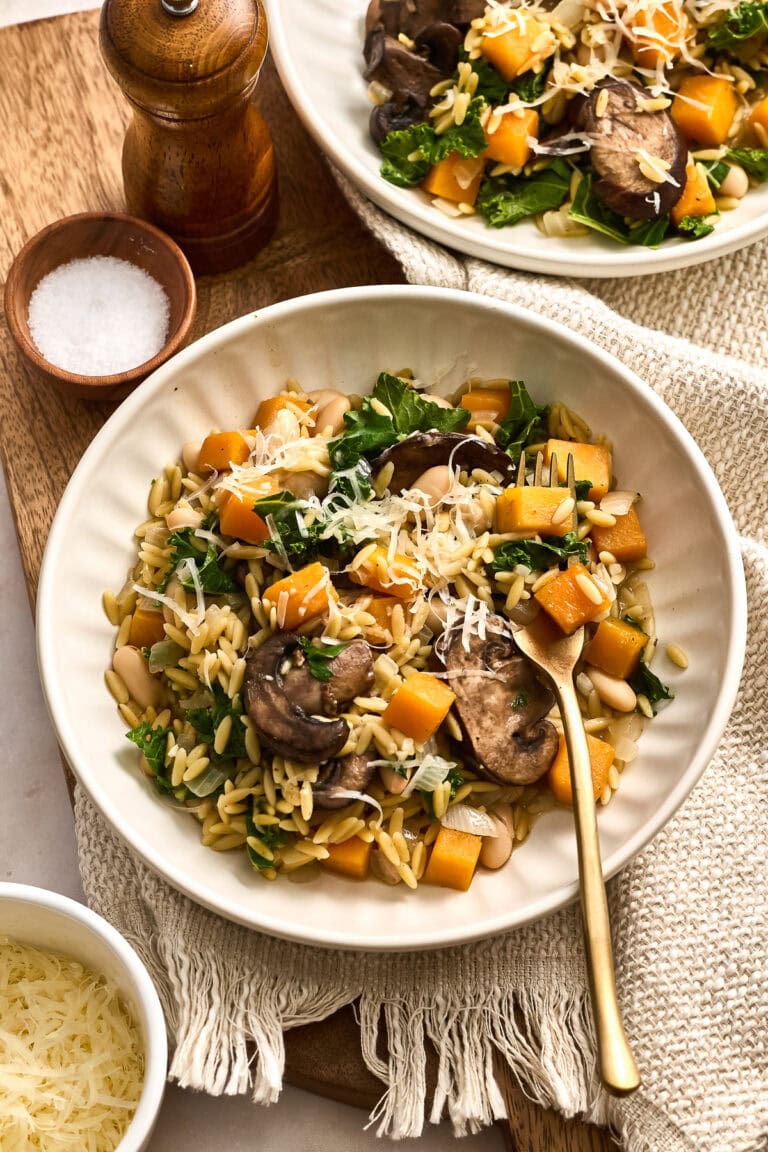 Delicious creamy butternut squash orzo with mushrooms, kale, and grated cheese served in a white bowl, perfect for a cozy meal.