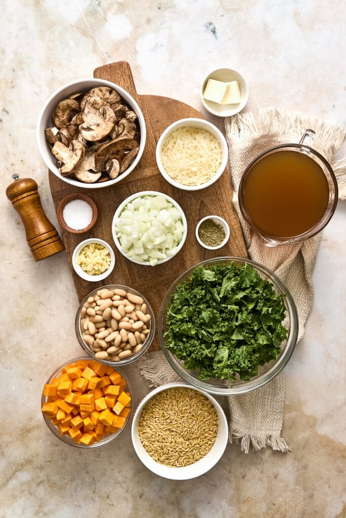 Assorted fresh ingredients for Creamy Butternut Squash Orzo with Mushrooms and Kale, including mushrooms, butternut squash, kale, orzo, and broth.