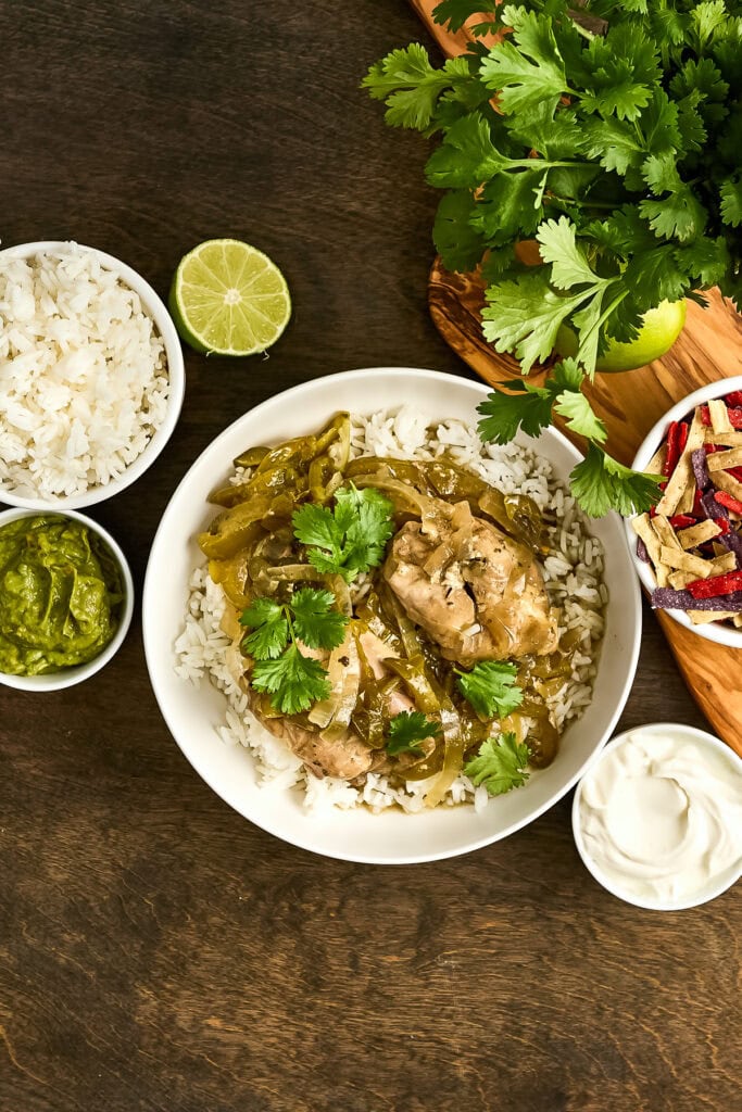 Delicious chicken in green sauce served over rice, garnished with fresh cilantro, accompanied by lime, salsa, and sour cream on a dark wooden table.
