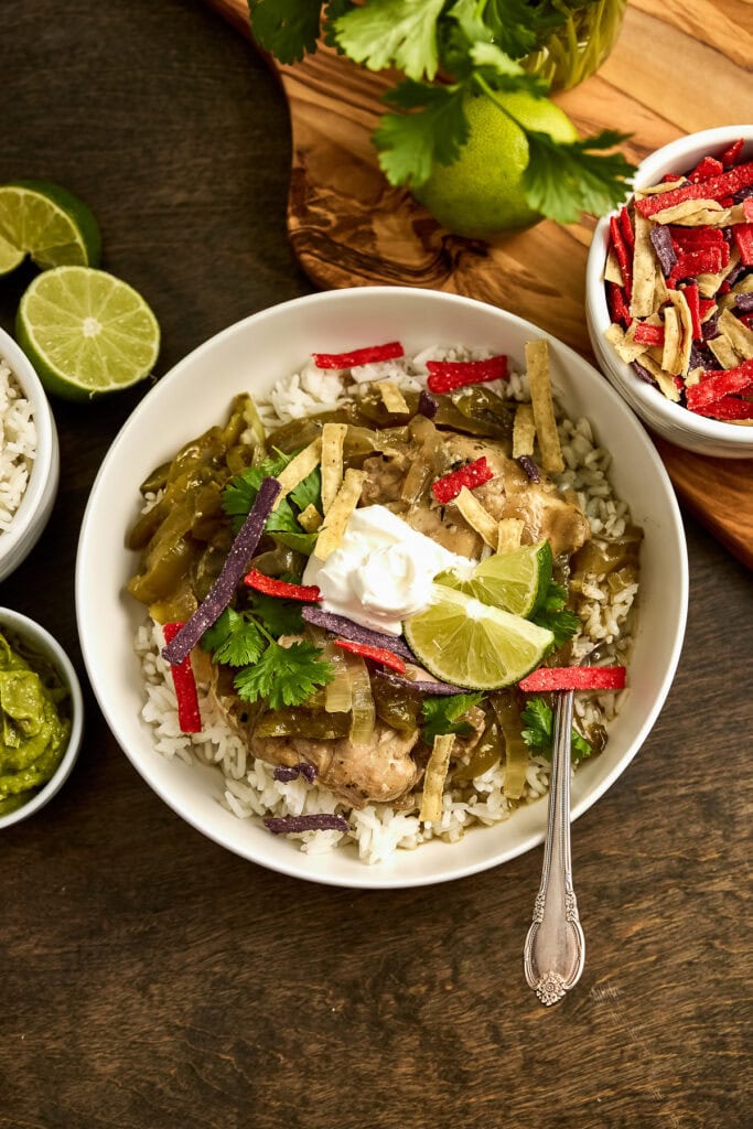 Delicious Mexican salsa verde chicken rice bowl with colorful peppers, lime, and sour cream, served in a white bowl on a wooden table with fresh lime and cilantro.