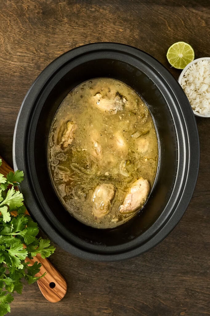 Delicious homemade chicken soup in a slow cooker with herbs, lime, and rice on the side, perfect for comfort and nutrition.