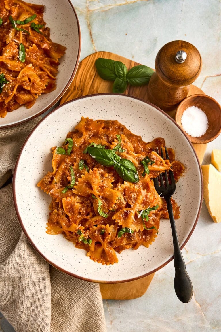 Bowl of creamy tomato ricotta pasta with ground beef, bowties and fresh basil