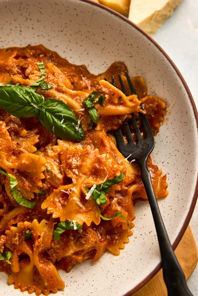 Close-up of creamy tomato ricotta pasts with ground beef, fresh basil, and grated cheese in a white bowl, served with a fork.