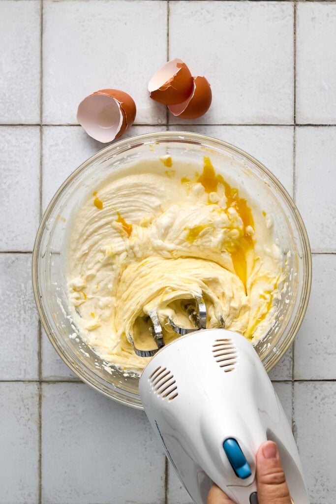 Mixing bowl with creamy batter and cracked eggshells on a tiled surface, ready for baking.
