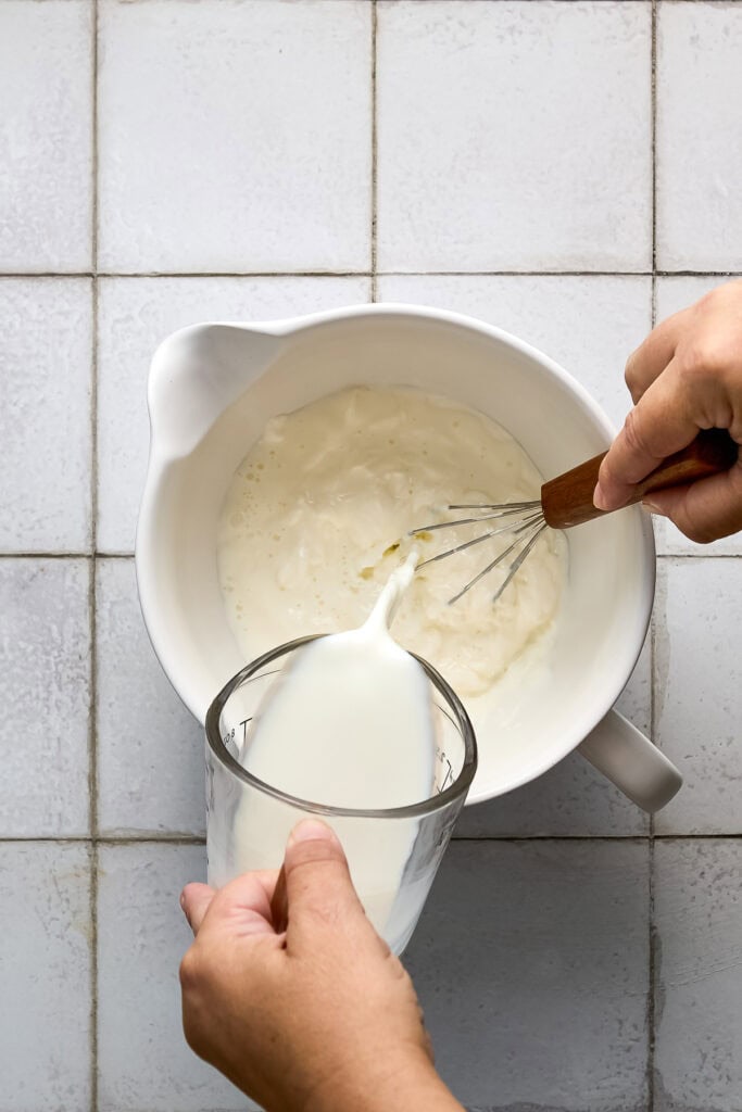hand whisking milk into a white bowl with sour cream.