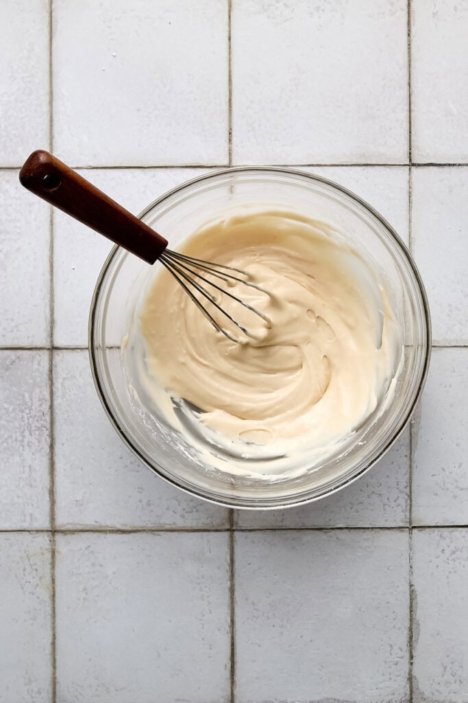 vanilla icing in a white bowl with a whisk.