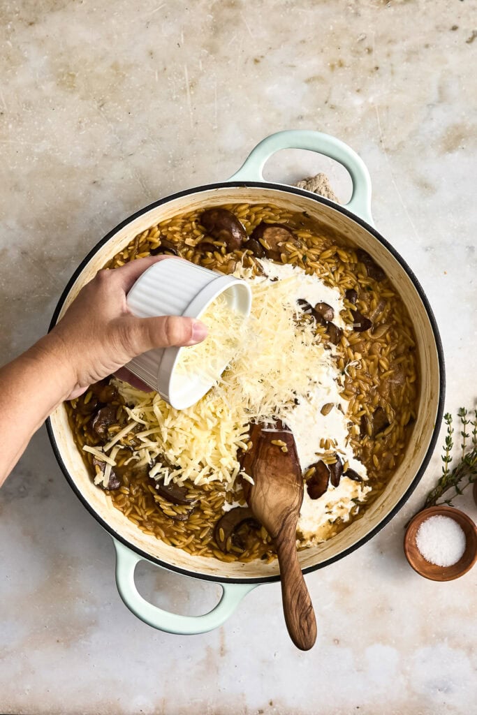 Cooking cheesy French onion pasta in a skillet with grated cheese, mushrooms, and creamy sauce, ready to serve.