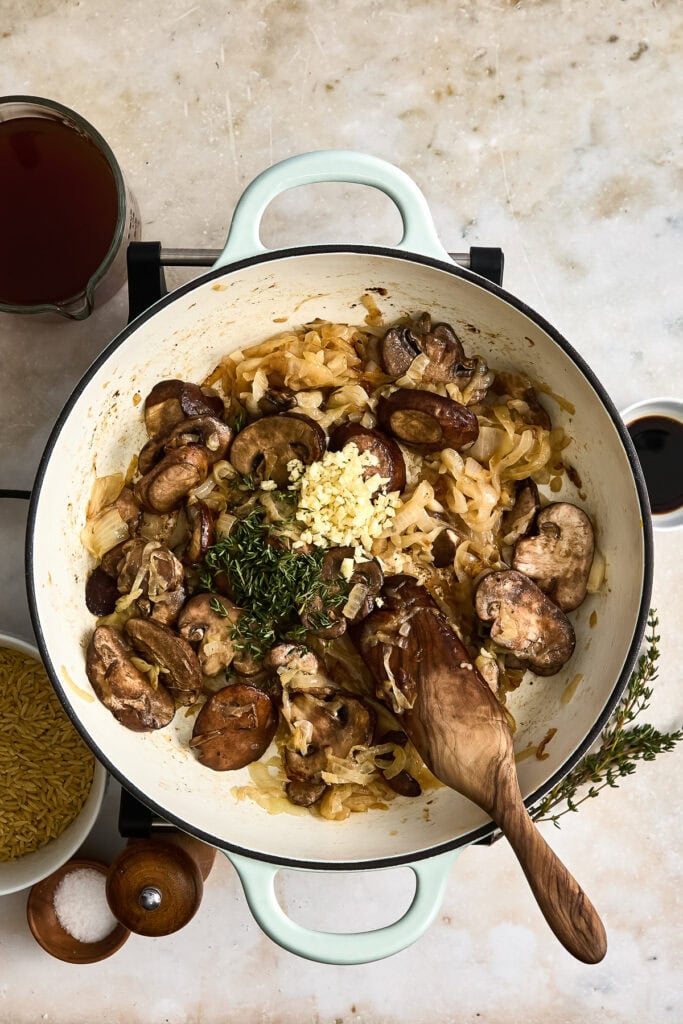 Close-up of a creamy a skillet with caramelized mushrooms and onions with herbs, and side dishes on a rustic table.